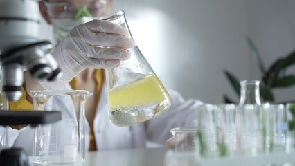 A scientist wearing white protective gloves is shaking up a yellow chemical solution inside an...