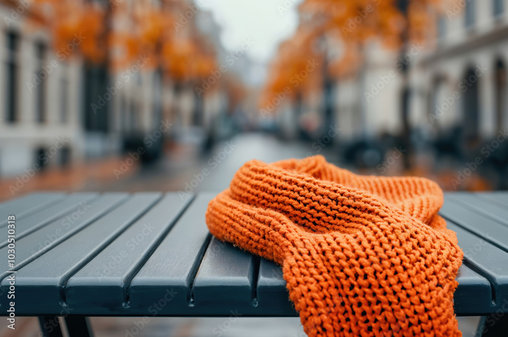 Aufkleber orange knitted scarf is lying on an empty bench against the backdrop of a blurred autumn city