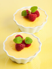 two bowls of vanilla custard garnished with raspberies and mint leaves