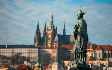 Naklejka premium Statue of St. John of Nepomuk overlooking the majestic Prague Castle on a clear day