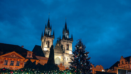 Christmas lights illuminate the towers of Týn Church against a twilight sky in Prague during the holiday season