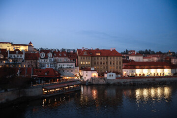 Naklejka premium Twilight view of riverfront buildings and rooftops in Prague showcasing historic architecture and serene reflections