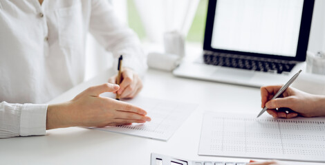 Two accountants using a calculator and laptop computer for counting taxes at white desk in office. Teamwork in business audit and finance