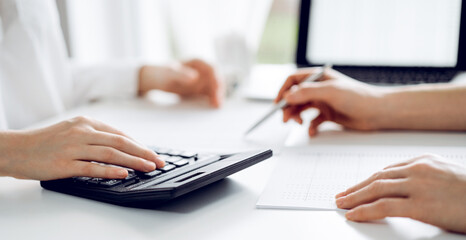 Two accountants using a laptop computer and calculator for counting taxes at white desk in office. Teamwork in business audit and finance