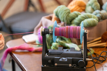 An electric eel wheel to spin colorful pink wool into handspun textured yarn on a wooden table....
