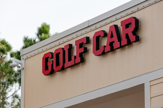 An electric channel letter sign or halo lit with bright red letters. The sign board and golf cart are attached to the exterior of a cream building with white trim. The business sign has black trim. - Powered by Adobe