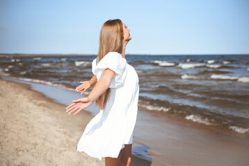 Happy smiling beautiful woman is on the ocean beach in a white summer dress, open arms