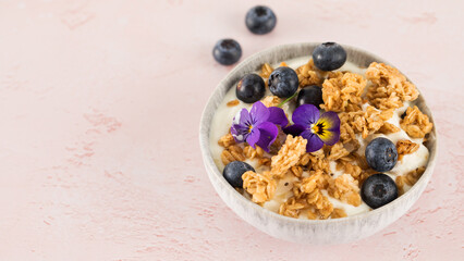 A healthy nutritious breakfast of natural Greek yoghurts, granola and fresh berries on pink background. Copy space