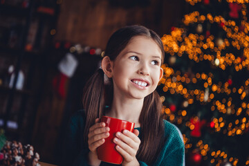 Photo of cute little girl drink cacao look empty space dressed green christmas outfit day light home party decoration interior room