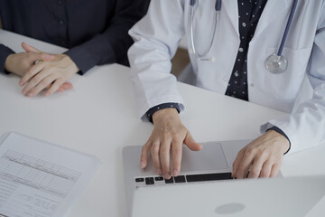 Doctor and a patient in clinic. The female physician is using laptop computer for filling up medication history record form, view above. Medicine and science