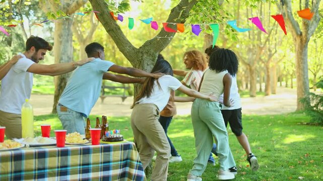 Friends playing conga line around tree at birthday party