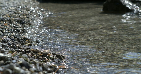 Pebble shoreline with sparkling water ripples in slow motion at 800 fps, capturing the serene beauty of a rocky lakeside, ideal for nature and tranquility themes