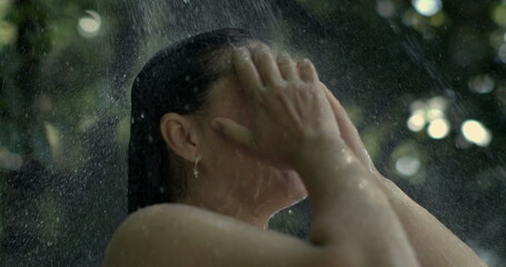 Woman enjoying cool outdoor shower, hands on face, refreshing spray in slow-motion at 800 fps, summer relaxation, natural environment, serene moment