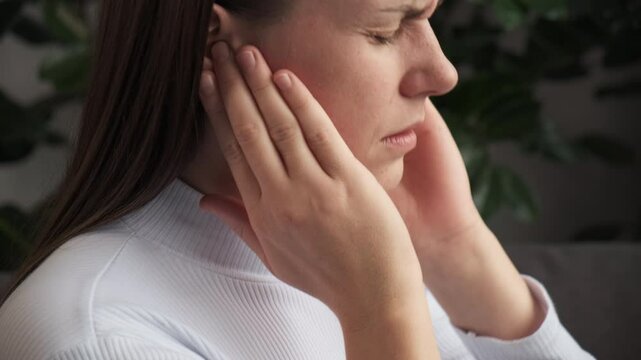 Tinnitus concept. Sick young woman sit on couch have ear pain or earache, hand touch plug ear, suffering painful otitis from loud of noisy sound, inflammation. Health care nerve deaf eardrum disease