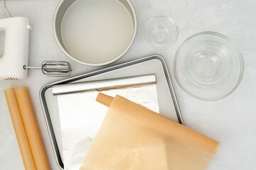 Flat lay composition featuring parchment paper, aluminum foil, a baking pan, mixer, and glass bowls...
