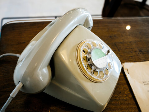 A vintage cream-colored rotary telephone sitting on a wooden desk, evoking nostalgia and classic communication methods from the mid-20th century