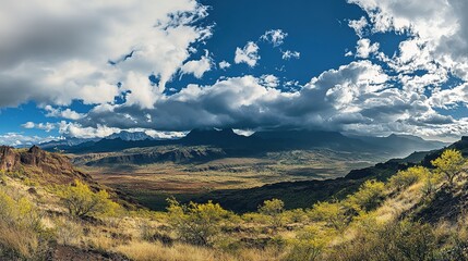Fototapeta premium A panoramic view of a vast valley surrounded by majestic mountains and dynamic clouds under a bright blue sky in a remote landscape