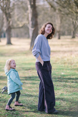 Fototapeta premium Young beautiful mother and adorable ginger-haired small daughter are playing together in a park