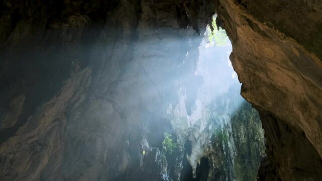 Sunlight streaming through Batu cave opening, illuminating the rugged rock formations and casting a mystical glow, creating a serene and mysterious atmosphere, Kuala Lumpur, Malaysia