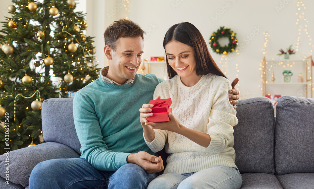 Wall mural wife opens a gift box from husband during christmas or new year at home. they celebrate the holiday 