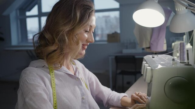 Smiling seamstress works diligently at her sewing machine in a workshop, skillfully sewing a piece of fabric with passion and dedication. The atmosphere reflects creativity and craftsmanship