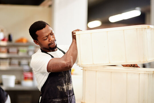 Black man, bakery and bucket with dispenser for mass production, stock or inventory of pastry at factory. Young African, male person or baker with apron or containers for food storage at warehouse