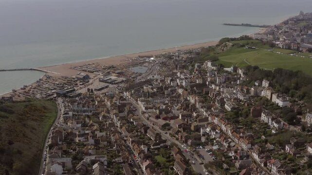 Aerial view of Hastings Old Town with with a detailed look at the seafront, townscape, pier and green hills on a cloudy day in England, UK