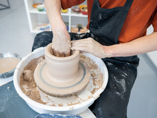 Close-up of a potter's hands making a ceramic vase on a potter's wheel. 
