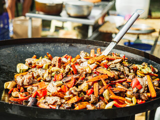 Street Food Festival: Man Stir-Frying Vegetables and Meat in a Large Pan at a Vibrant Urban Gathering