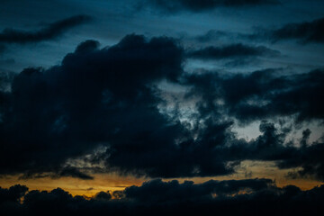 Dark, dramatic storm clouds dominate the sky at dusk, with faint traces of an orange sunset glowing on the horizon. The deep blue and black tones create a moody, atmospheric scene.