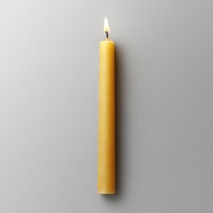 Tall yellow candle lit on a gray surface casting a soft glow.
