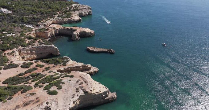 Aerial drone shot of boat at Benagil sea caves and Atlantic Ocean coastline in Benagil, Algarve, Portugal, Europe. Boats sightseeing in the Mediterranean. Shot in 5K ProRes 422 HQ