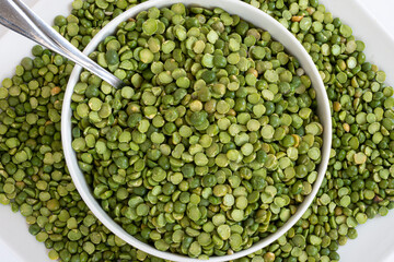 A top view image of split green peas and spoon in a white ceramic bowl white.