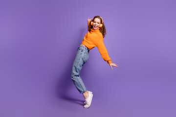 Full size photo of nice young girl stand tiptoe headphones wear pullover isolated on violet color background