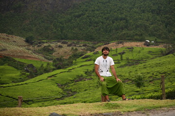 Naklejka premium Happy smiling man solo traveller sitting in the mountains of Munnar, on tea plantations in India