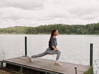 Determined Asian woman practicing yoga on wooden deck by the serene lake, focusing on her poses and inner peace Wellness and fitness concept