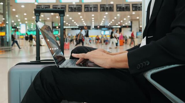 Businessman Uses Laptop, Waiting for a Flight in Airport Terminal or train station, Traveling Entrepreneur Working Online On Computer Sitting in a Boarding Lounge of Airline Hub with Airplanes