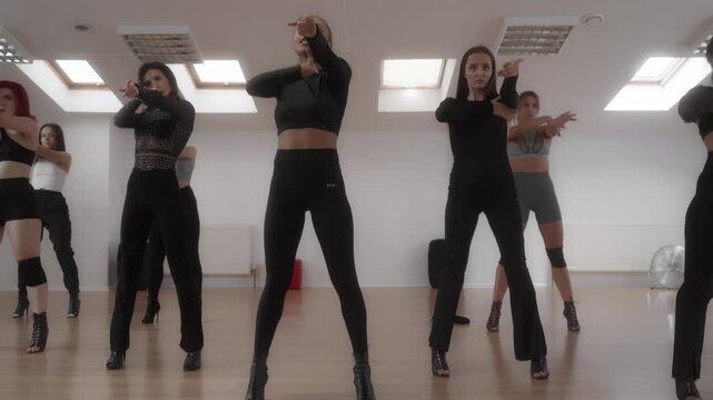 A team of dancers rehearses a dance together in the dance studio. A group of women practices expressive dance moves during a dance class. The High Heels choreography classes are designed for adults.