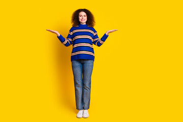 Full size photo of positive woman dressed striped sweater palms comparing products empty space isolated on yellow color background