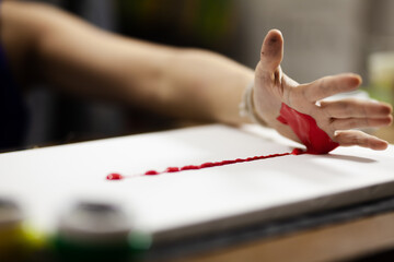 Female artist making an artistic painting with red color on her hand.