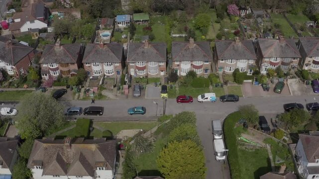 Aerial shot tracking down a suburban residential street with 1930s houses, gardens and parked cars in Hastings, UK