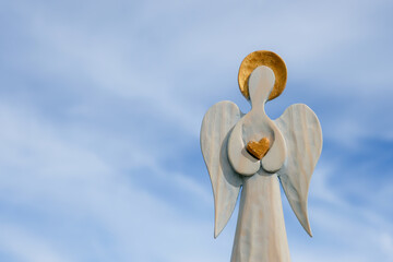 Angel wooden figure with a golden halo and heart. Blue sky background. Copy space.