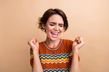 Photo of pretty delighted person closed eyes raise fists achieve shout yes hooray isolated on beige color background