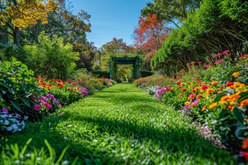 Fototapeta premium Wide-angle garden view with green lawn, colorful flowers, arbor, lush foliage, and varied trees in bright sunshine.