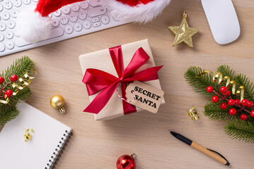 Top view of an office desk adorned with a wrapped gift, red ribbon, Santa hat, and festive decorations during the holiday season
