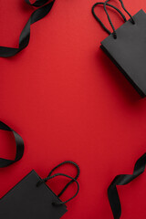 Black shopping vertical bags with handles on a bright red backdrop, representing Black Friday sales...