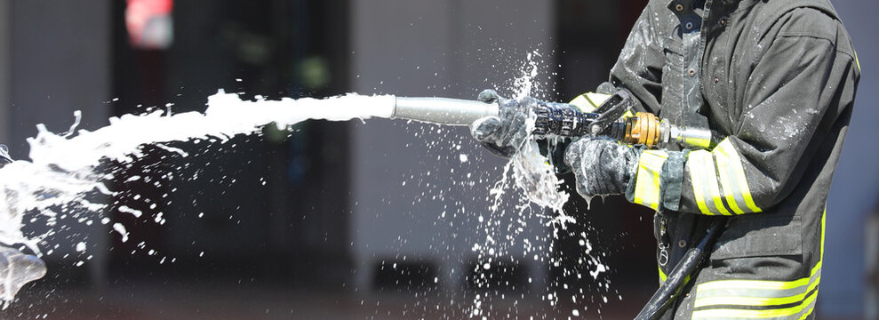 firefighter is spraying foam extinguishing agent with a powerful hose to control a fire