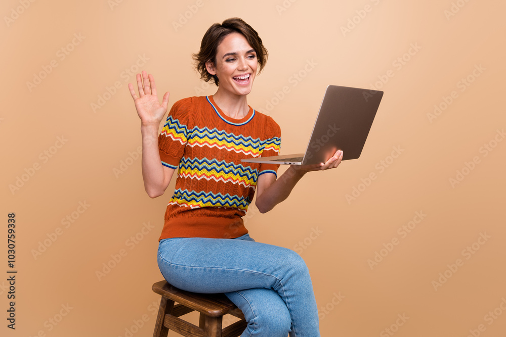 Poster Full body photo of cheerful pretty lady sit chair arm palm waving hi speak video call netbook isolated on beige color background