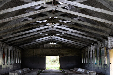 Interior of an abandoned isolated farm building with light peeking through a decaying roof. Building shows high contrast of interior versus light beams adding depth and eeriness to the scene.