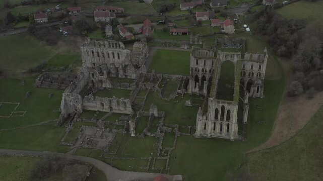 Drone shot of historic Rievaulx Abbey ruins surrounded by greenery and small buildings in Helmsley, England, UK